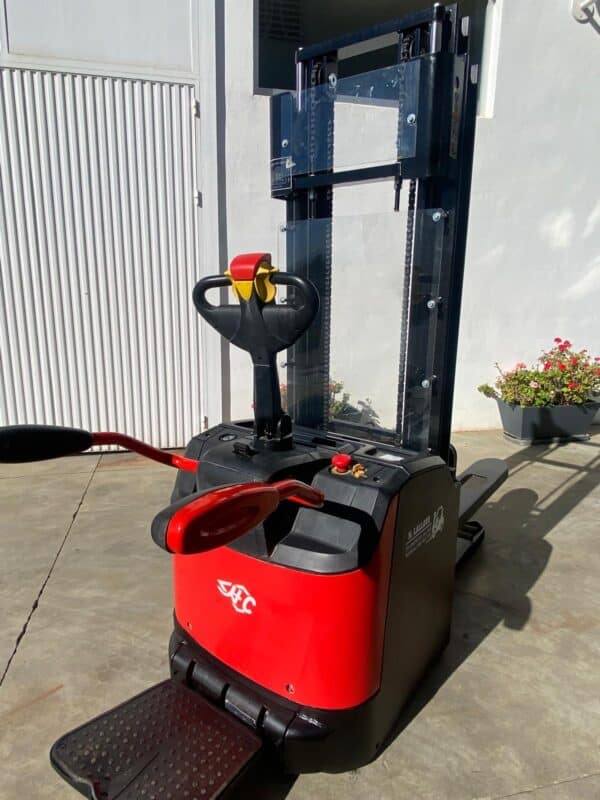 Apilador eléctrico de 1400kg en uso en almacén con palé y estanterías.