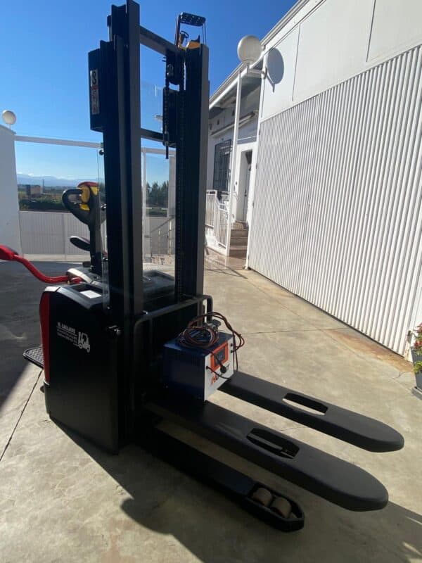 Apilador eléctrico de 1400kg en exteriores con horquillas largas y control ergonómico.